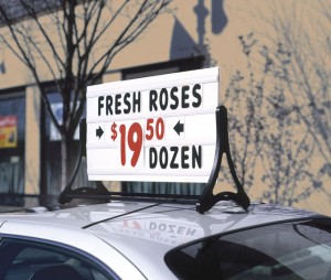 Fresh Roses advertised on a message board on top of a car parked in front of a store